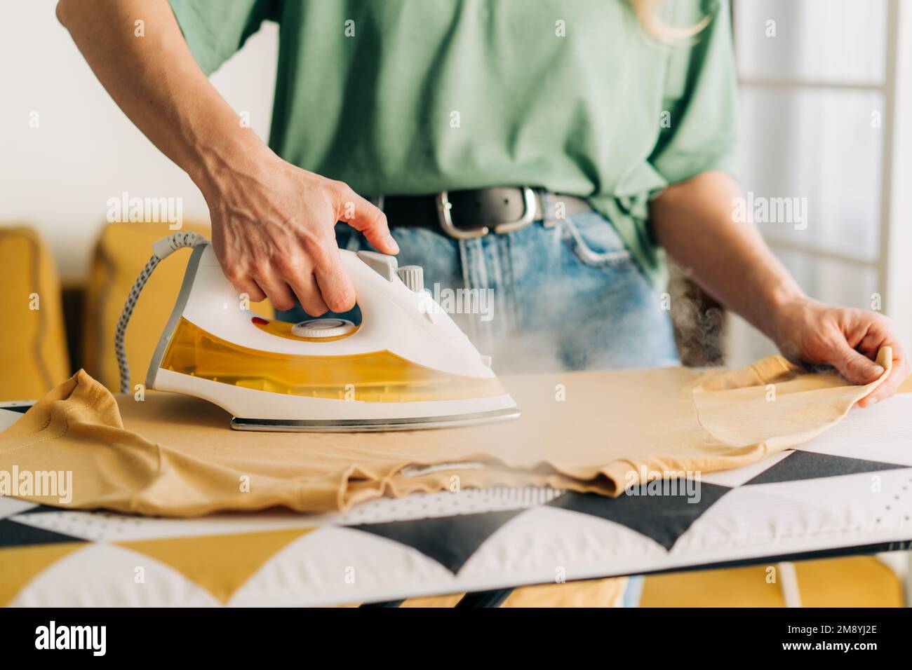 Close-up of an unrecognizable woman ironing clothes with steam on an ironing board. Stock Photo