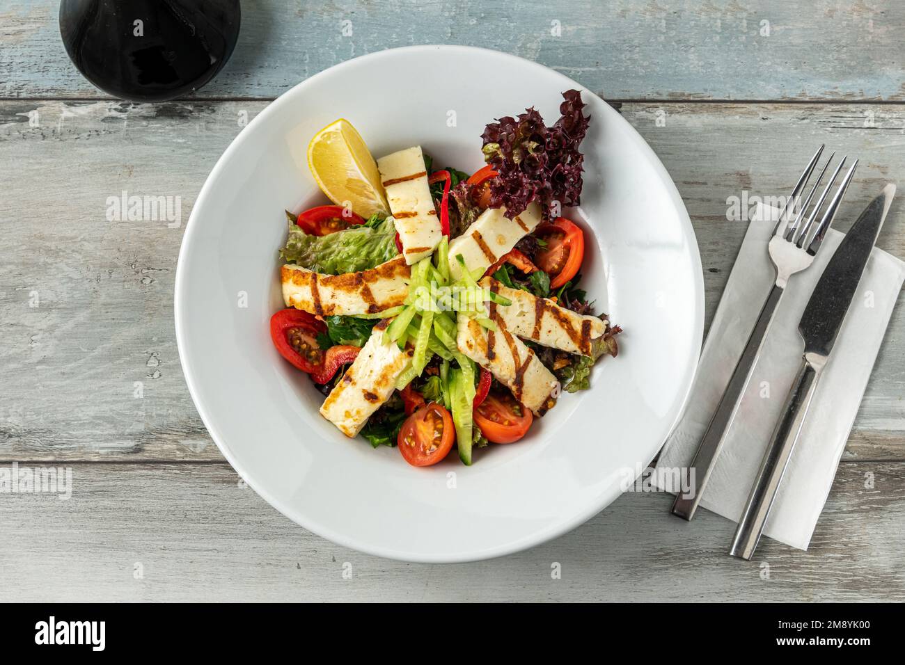 Salad with tomato and halloumi cheese on wooden table Stock Photo