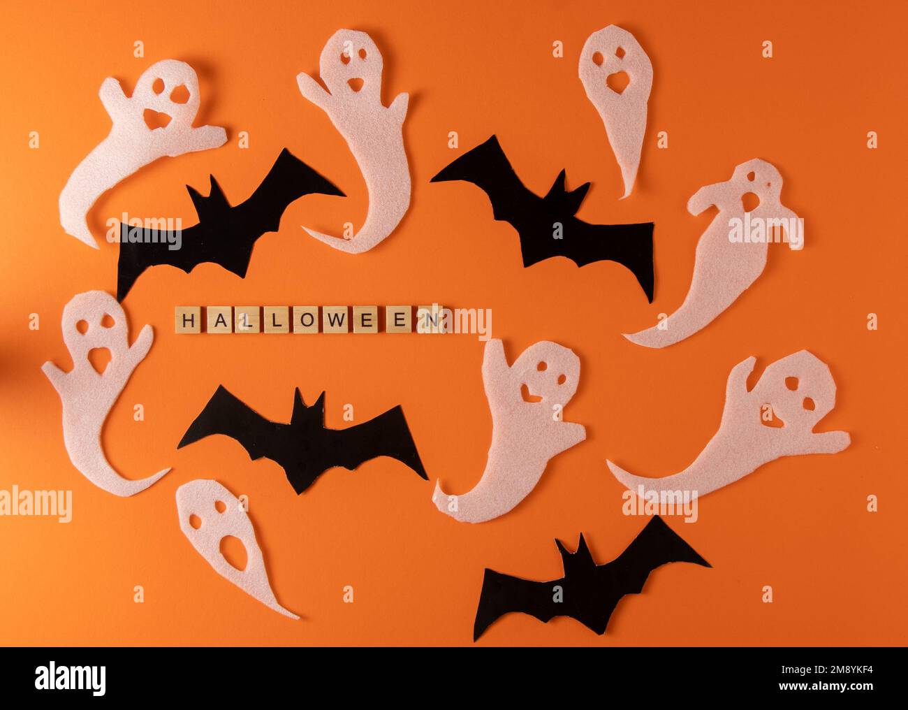White ghosts and bat craft for Halloween party. Wrapping paper ghost on orange background top view. Cartoon creepy Whisper. DIY hand made. Set boo characters. Word wooden letter phrase. Stock Photo