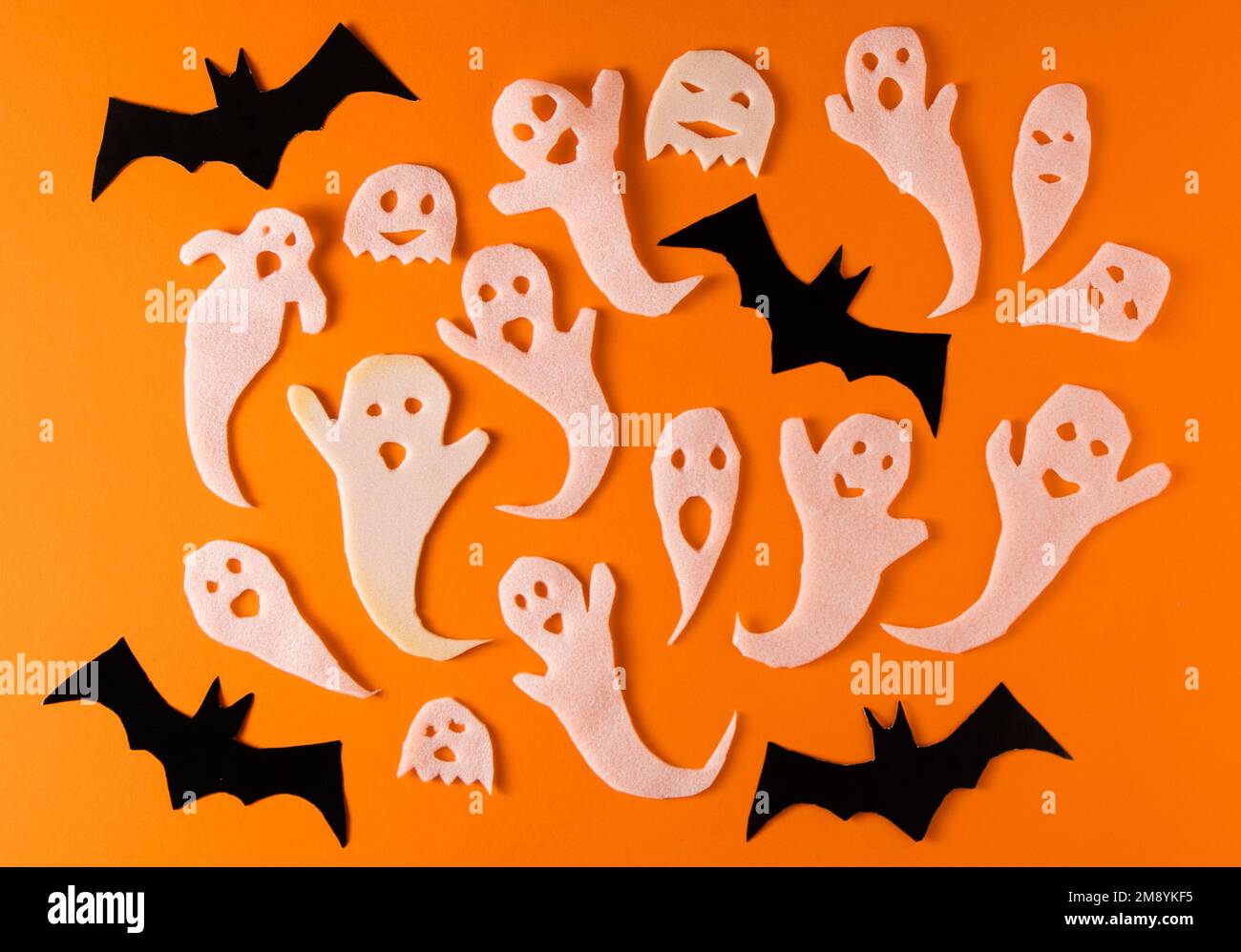 White ghosts and bat craft for Halloween party. Wrapping paper ghost on orange background top view. Cartoon creepy Whisper. DIY hand made. Set boo characters. Stock Photo