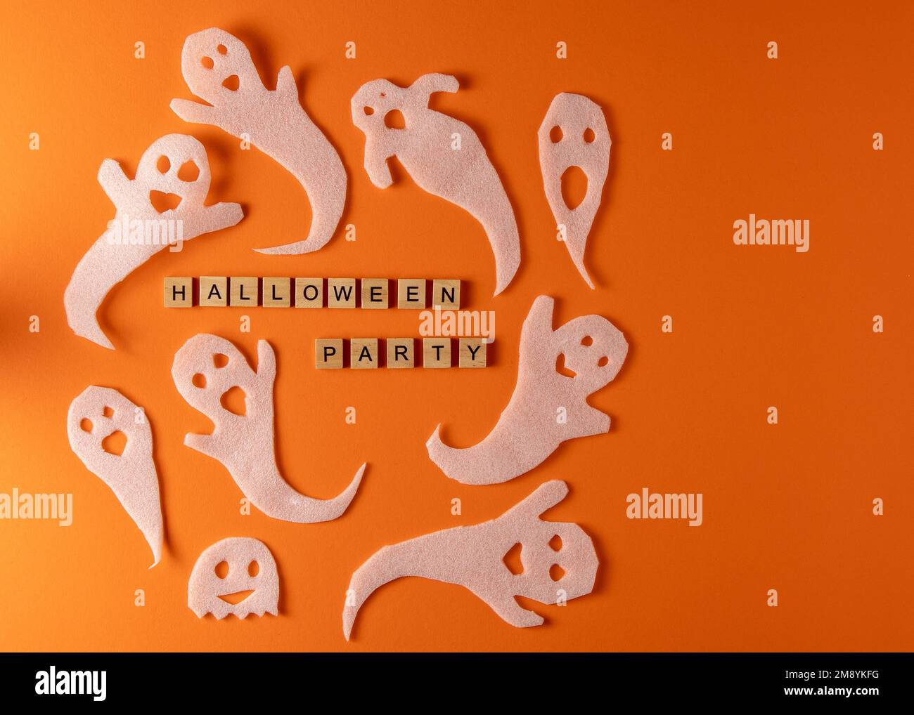 White ghosts craft for Halloween party. Wrapping paper ghost on orange background top view. Cartoon creepy Whisper. DIY hand made. Set boo characters. Word wooden letter phrase. Stock Photo