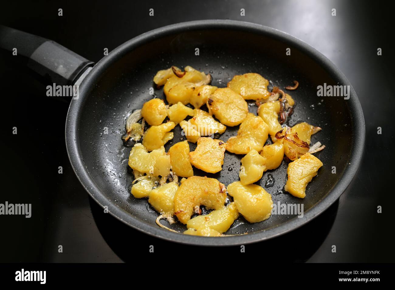 Potato slices and onion are roasted in a black frying pan on the stove, in Germany called Bratkartoffeln, food and cooking theme, selected focus, narr Stock Photo