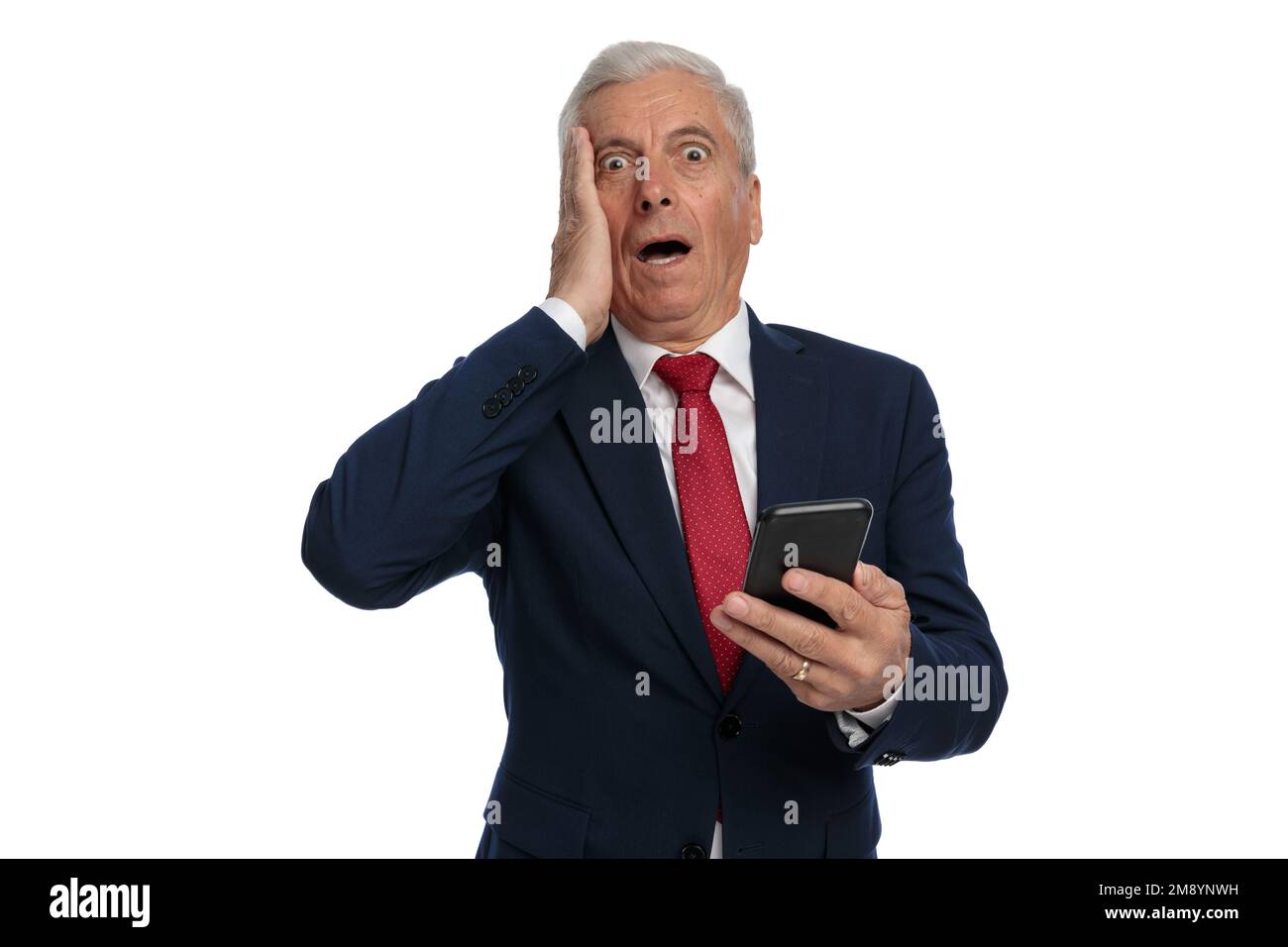 Old businessman slapping his face feeling utterly shocked while holding his mobile phone Stock Photo