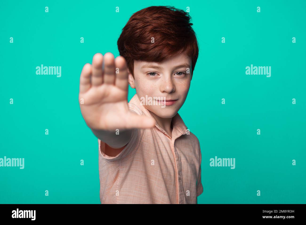 Little boy standing with outstretched hand showing stop sign, preventing you isolated over green backgrpund. Stock Photo