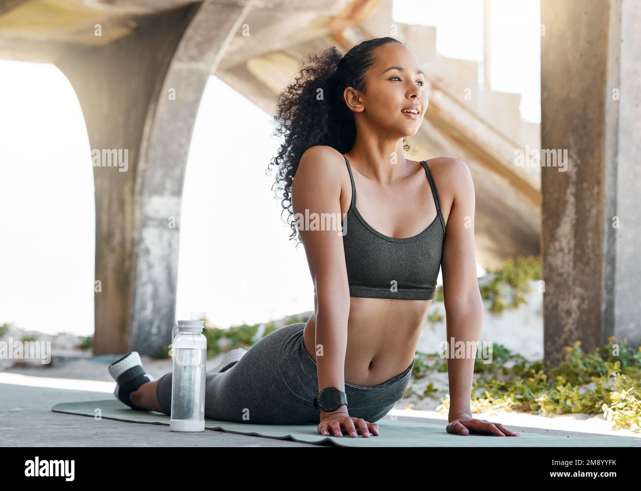 Releasing all that tension. Full length shot of an attractive young woman holding an upward facing dog pose while practicing yoga in the city. Stock Photo