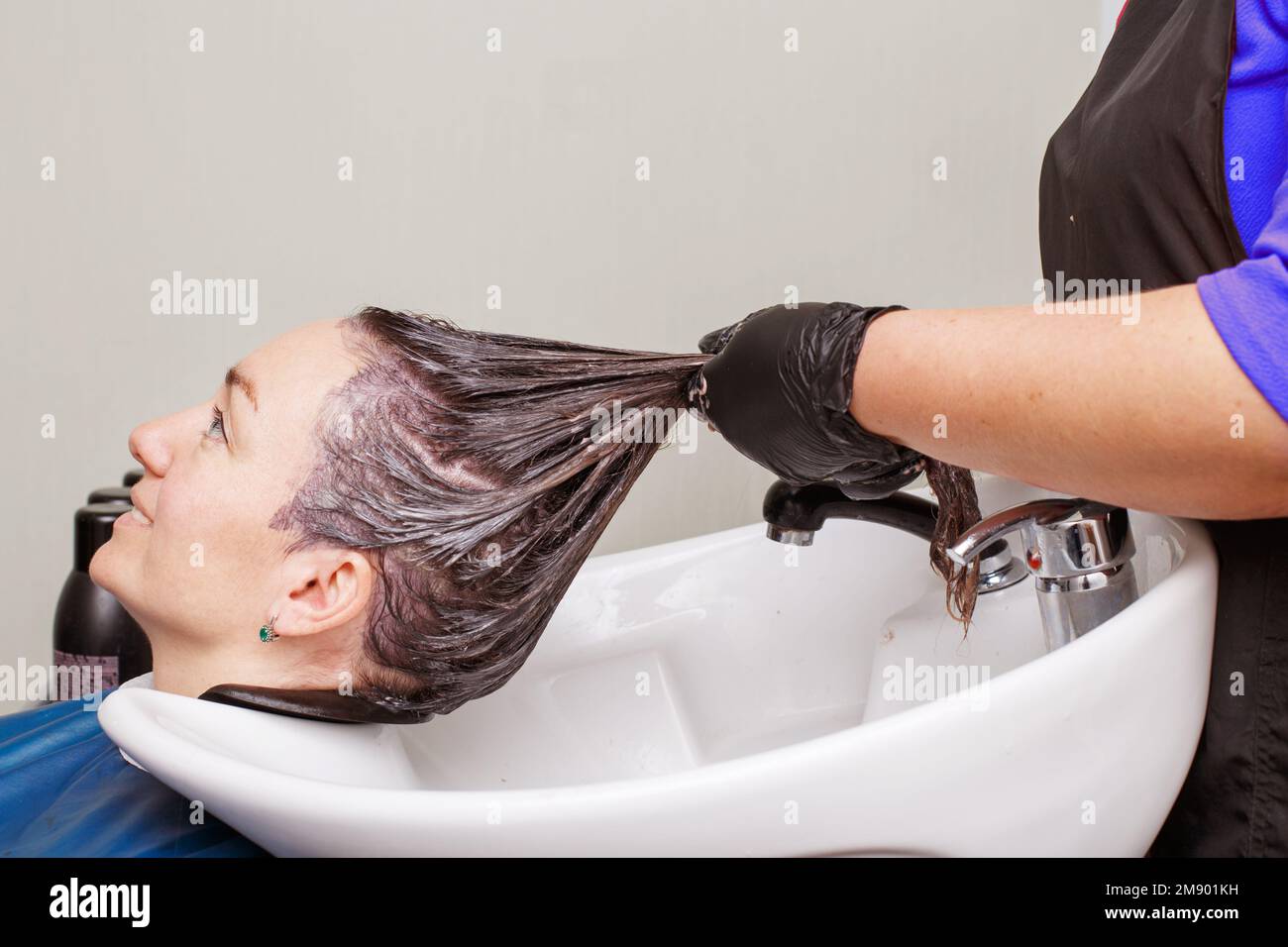 The hairdresser in black gloves washing woman's hair in the