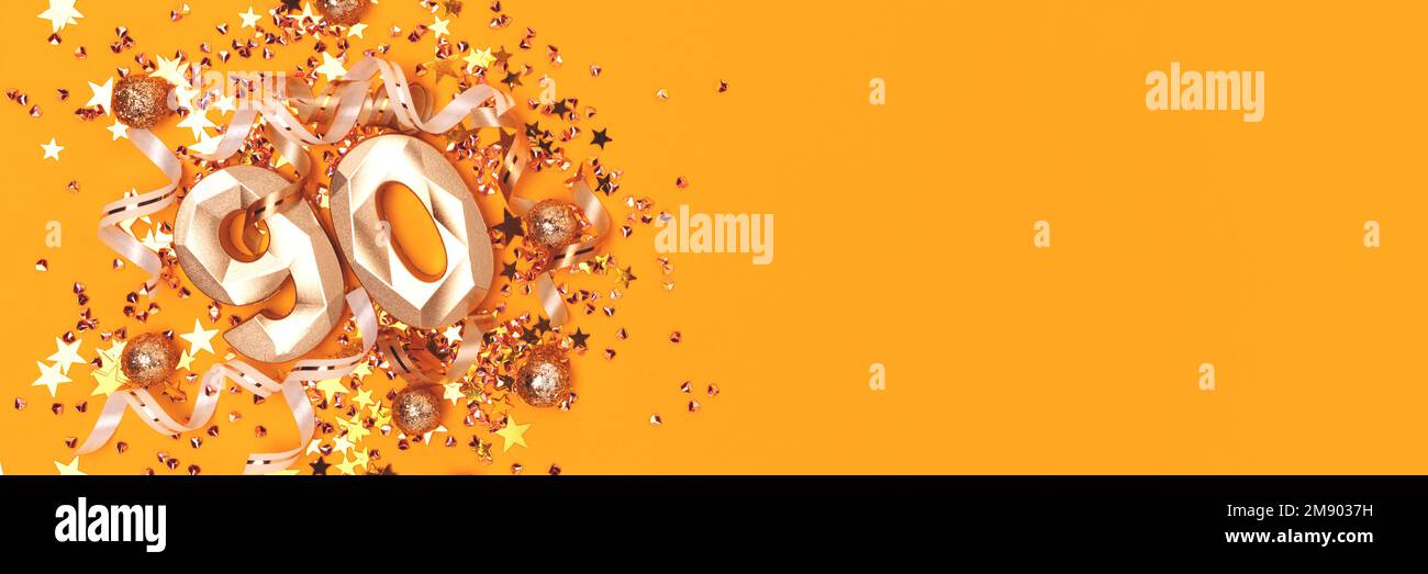 Banner with gold colored number 90, ribbons and glittering stars confetti on a yellow background. Place for text. Stock Photo