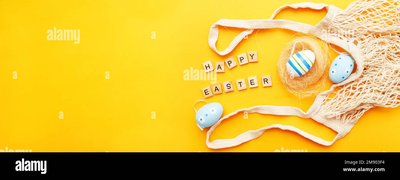 inscription happy easter with colorful handmade painted eggs and cotton string bag on orange background. banner Stock Photo