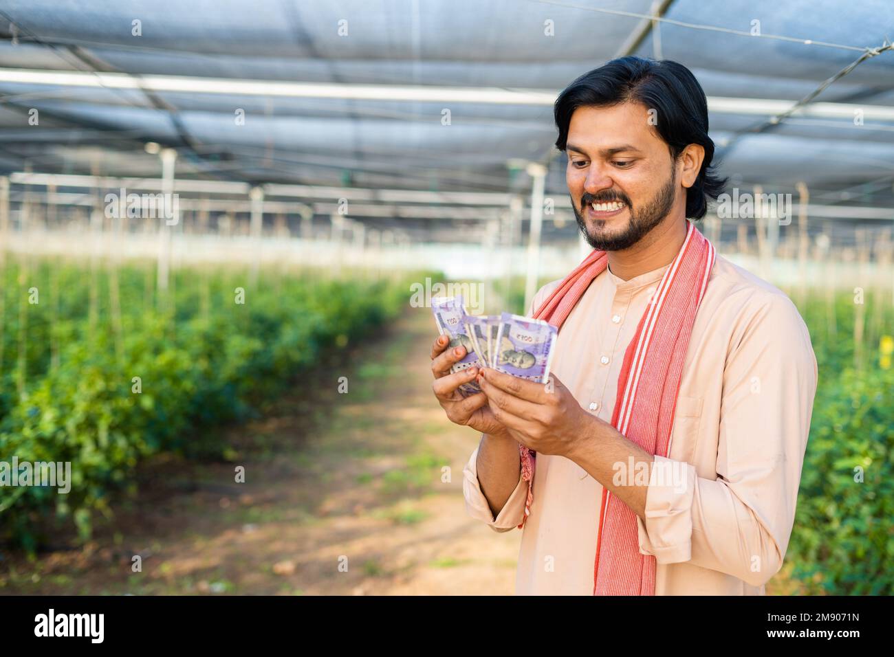 Happy smiling young farmer at greenhouse couting money or currency notes - concept of successful business, agronomy and financial or banking Stock Photo