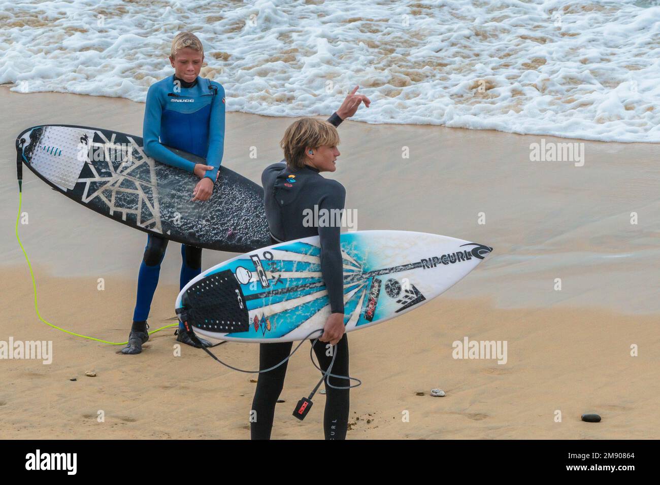 Young surfers carrying their surfboards standing on Fistral Beach in Newquay in Cornwall in England in the UK. Stock Photo