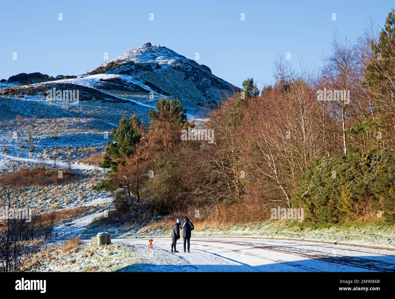 Holyrood Park, Edinburgh, Scotland, UK. 16th January 2023. Snow cover and icy roads and pavements in the Scottish capital, early morning temperature of minus 3 degrees centigrade. Pictured: A couple walk along the icy pavement with the summit of Arthur's Seat in background. Credit: ArchWhite/alamy live news. Stock Photo