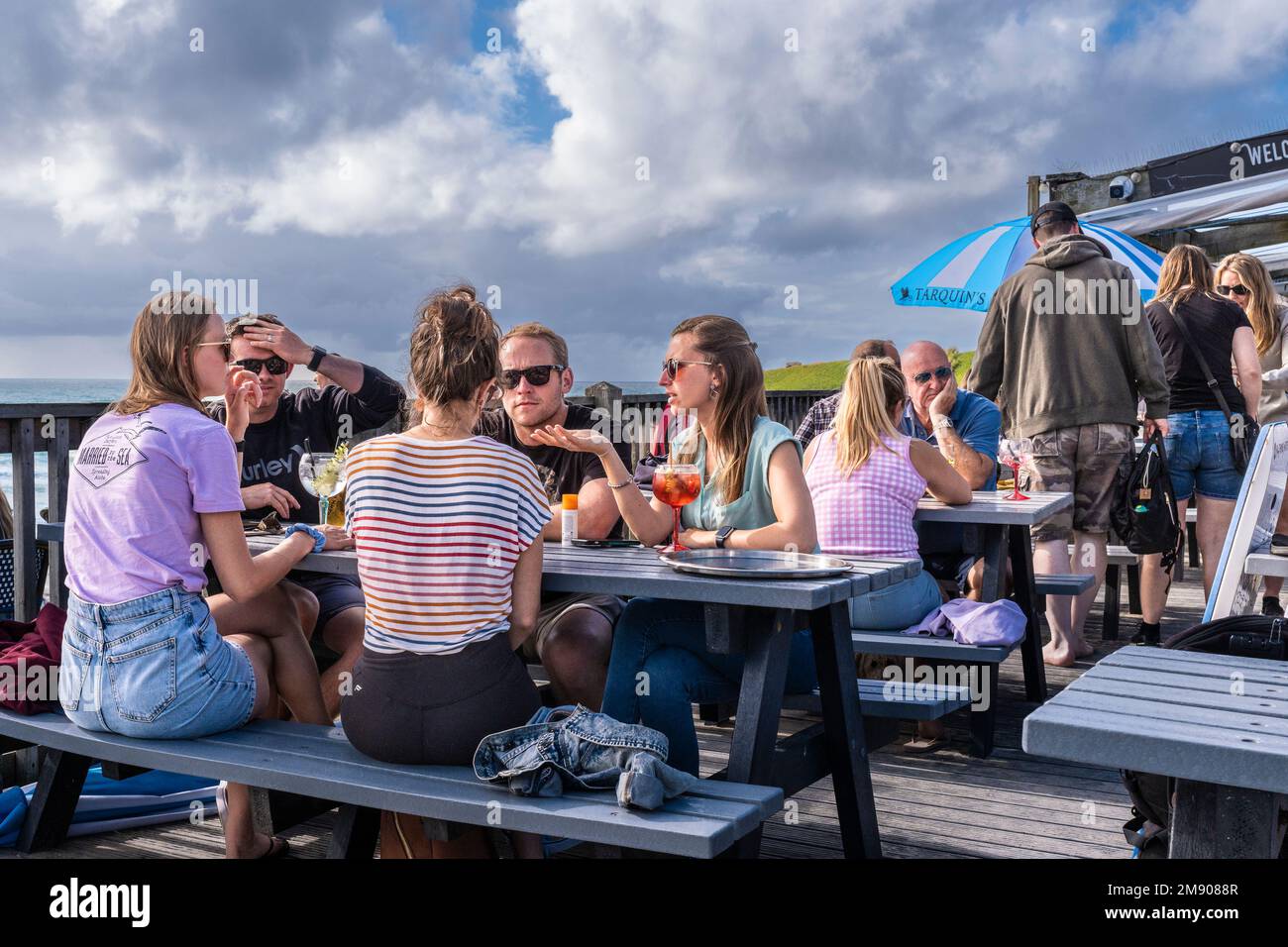 Holidaymakers drinking and socialising socializing on the decking area of Fistral Beach Bar in Newquay in Cornwall in England in the UK. Stock Photo