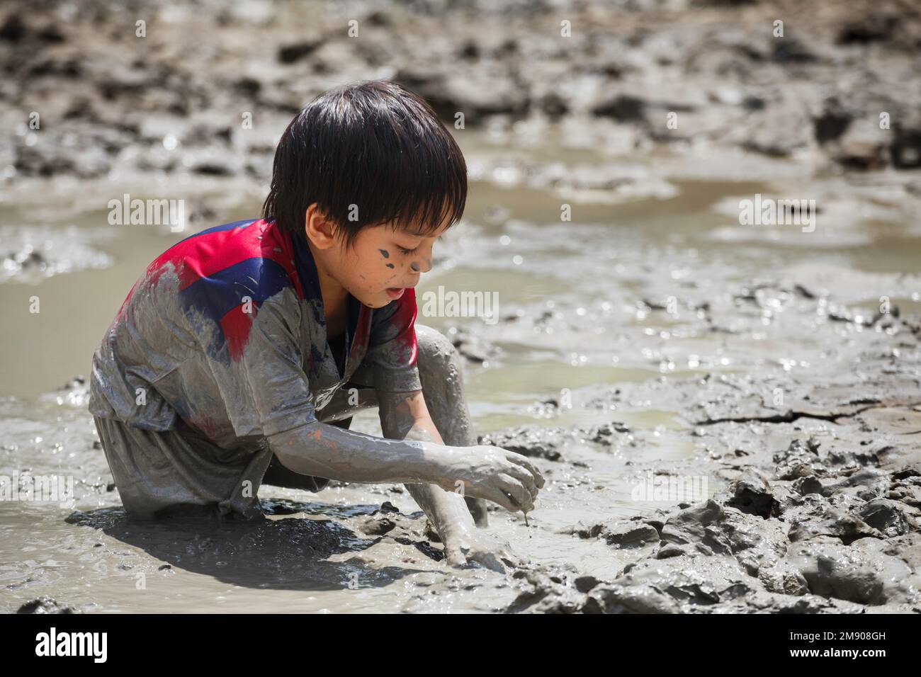 cute happy asian little boy enjoying to play in the mud at playground. child learning in nature at montessori school. nature and education concept. Stock Photo