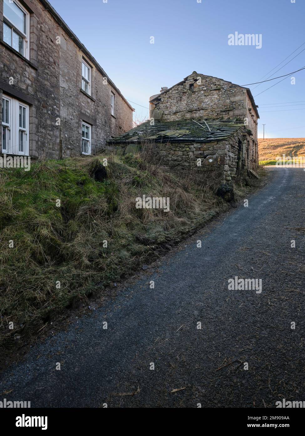 Cluster of farm buildings with bright blue sky ,distant hills and rough farm track in foreground Stock Photo