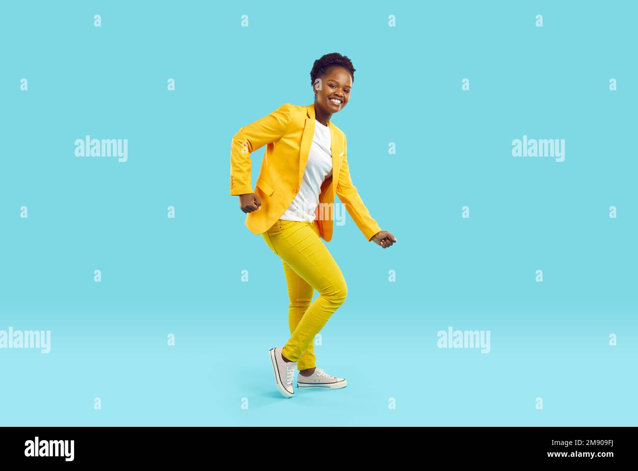 Happy beautiful African American woman in yellow suit dancing on blue background Stock Photo