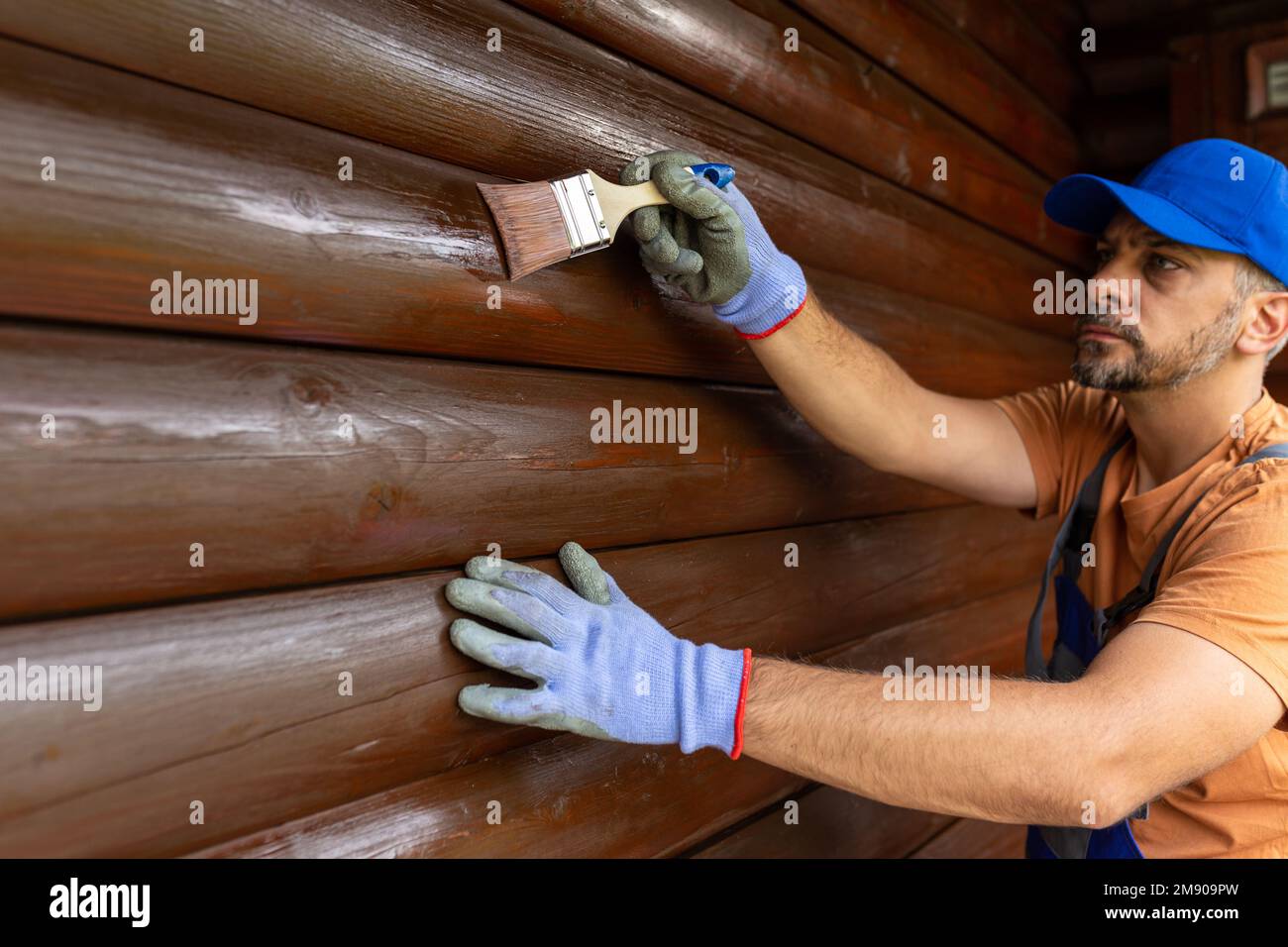 Wooden house maintenance concept. Man staining wall siding trunk Stock
