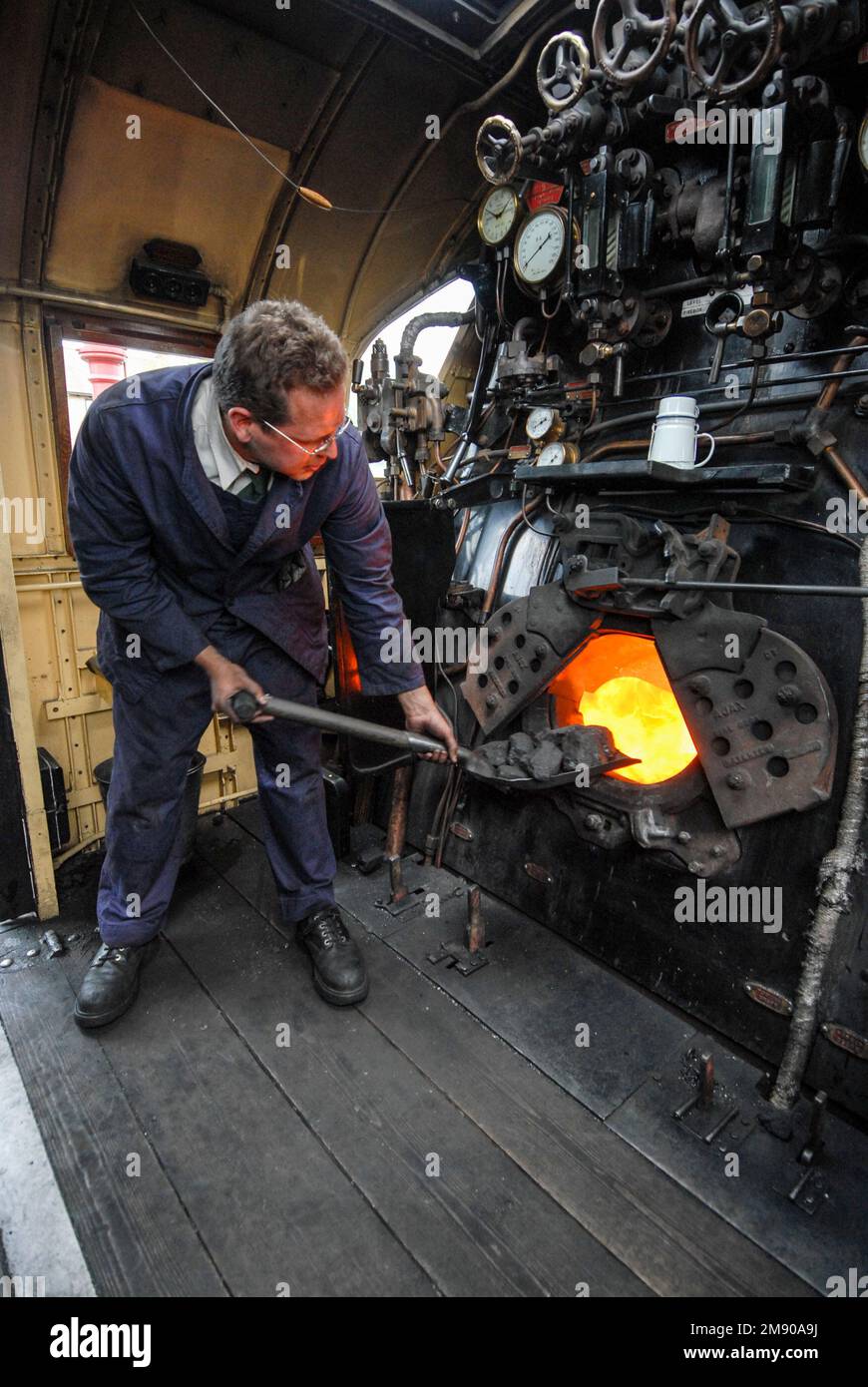 A steam engine fireman using a shovel, stoking coal into the steam train furnace at Winchcombe station in the Cotswolds in Britain.  It is part of the Stock Photo