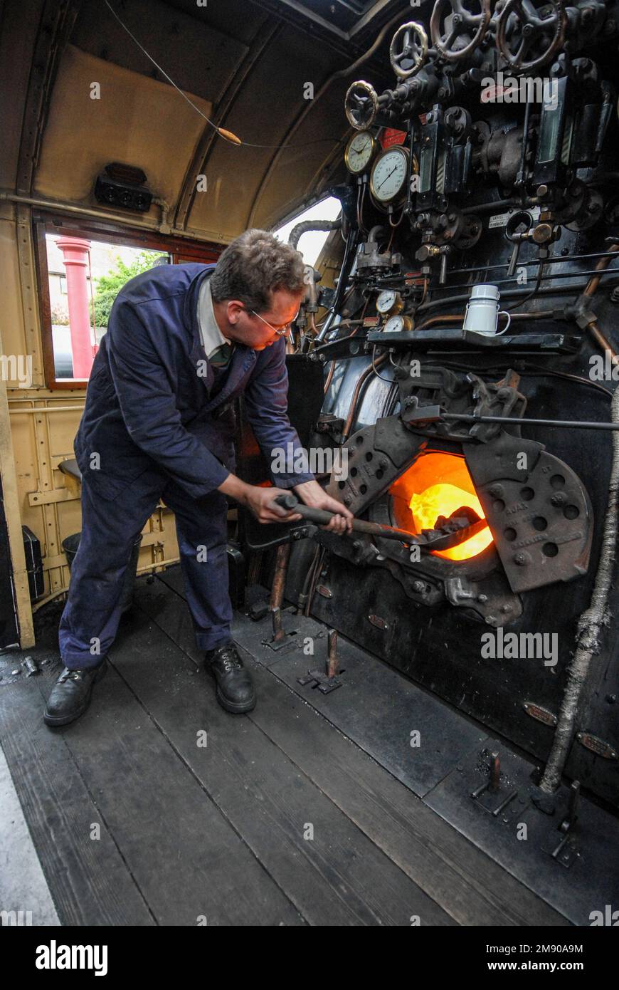 A steam engine fireman using a shovel, stoking coal into the steam train furnace at Winchcombe station in the Cotswolds in Britain.  It is part of the Stock Photo