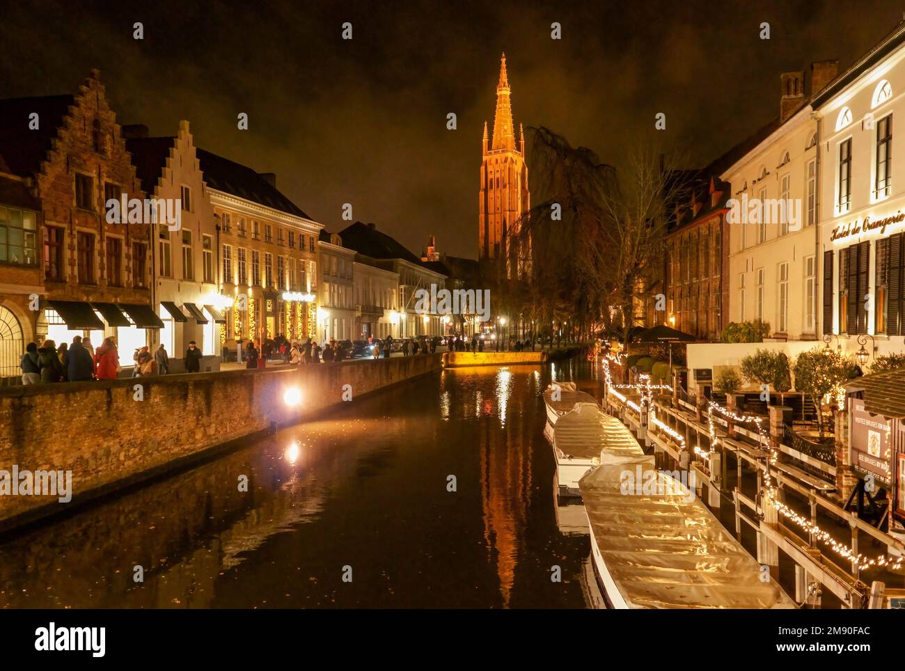 Tourist boats moored up at night along the canal with St Salvator's Cathedral tower in the background, Bruges Belgium. November 2022. Stock Photo