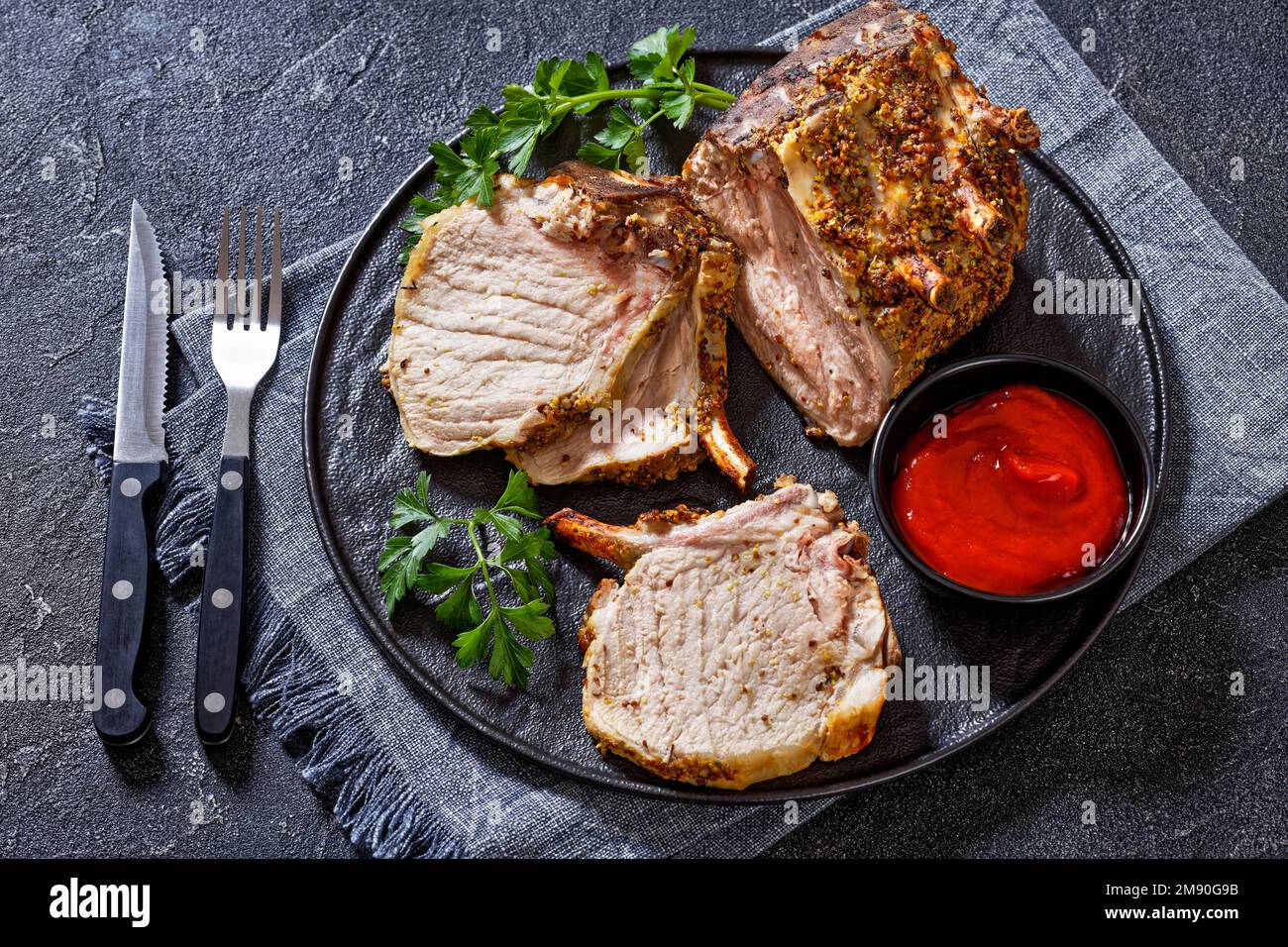 Standing Pork Rib Roast cut  on chops on black plate with  tomato sauce and parsley, horizontal view from above Stock Photo