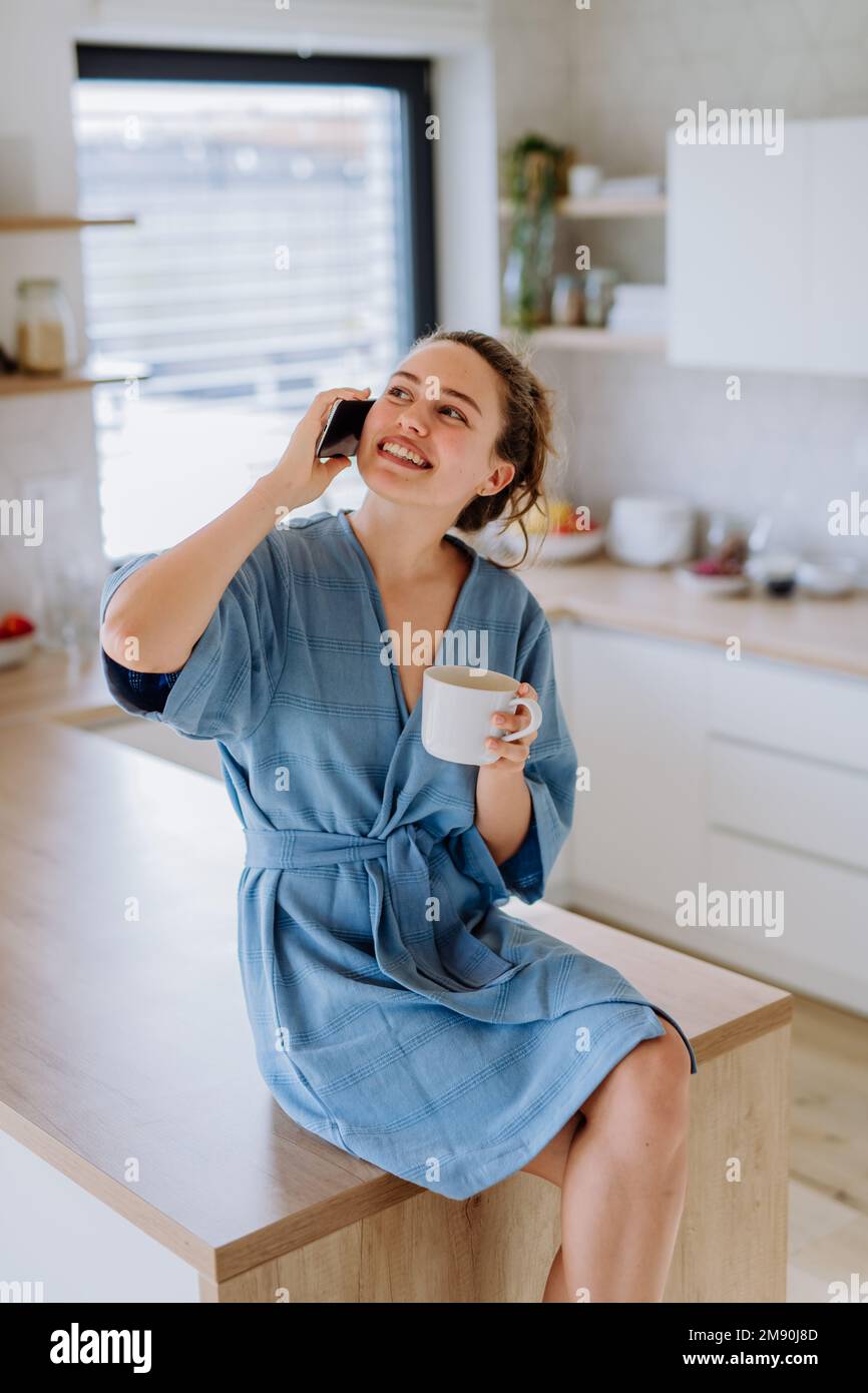 Young woman calling and enjoying cup of coffee at morning, in her kitchen. Stock Photo