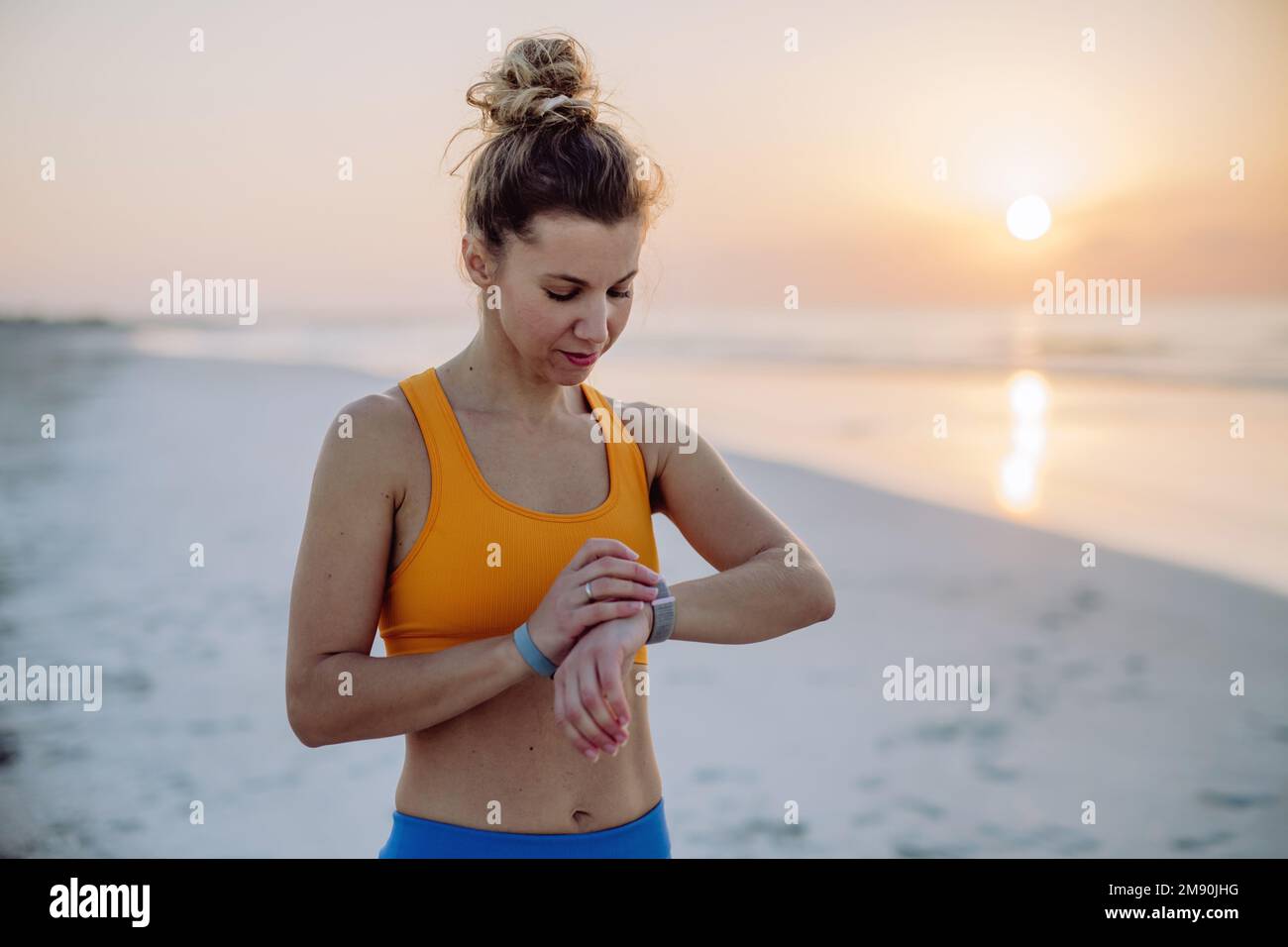 Young woman taking exercises at beach and checking her smartwatch, morning routine and healthy lifestyle concept. Stock Photo