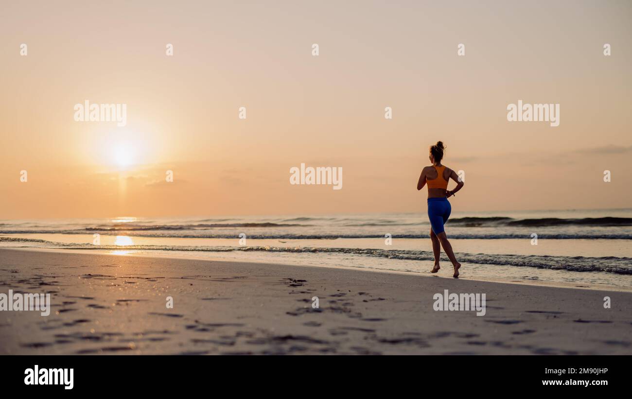 Rear view of young woman running at beach, morning routine and healthy lifestyle concept. Stock Photo