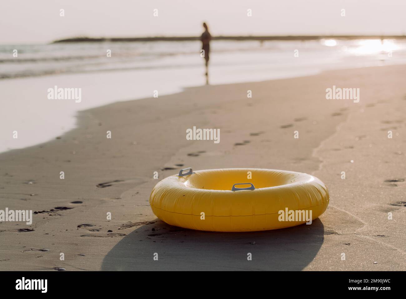 Close-up of yellow inflatable wheel on the beach, with person in background. Stock Photo