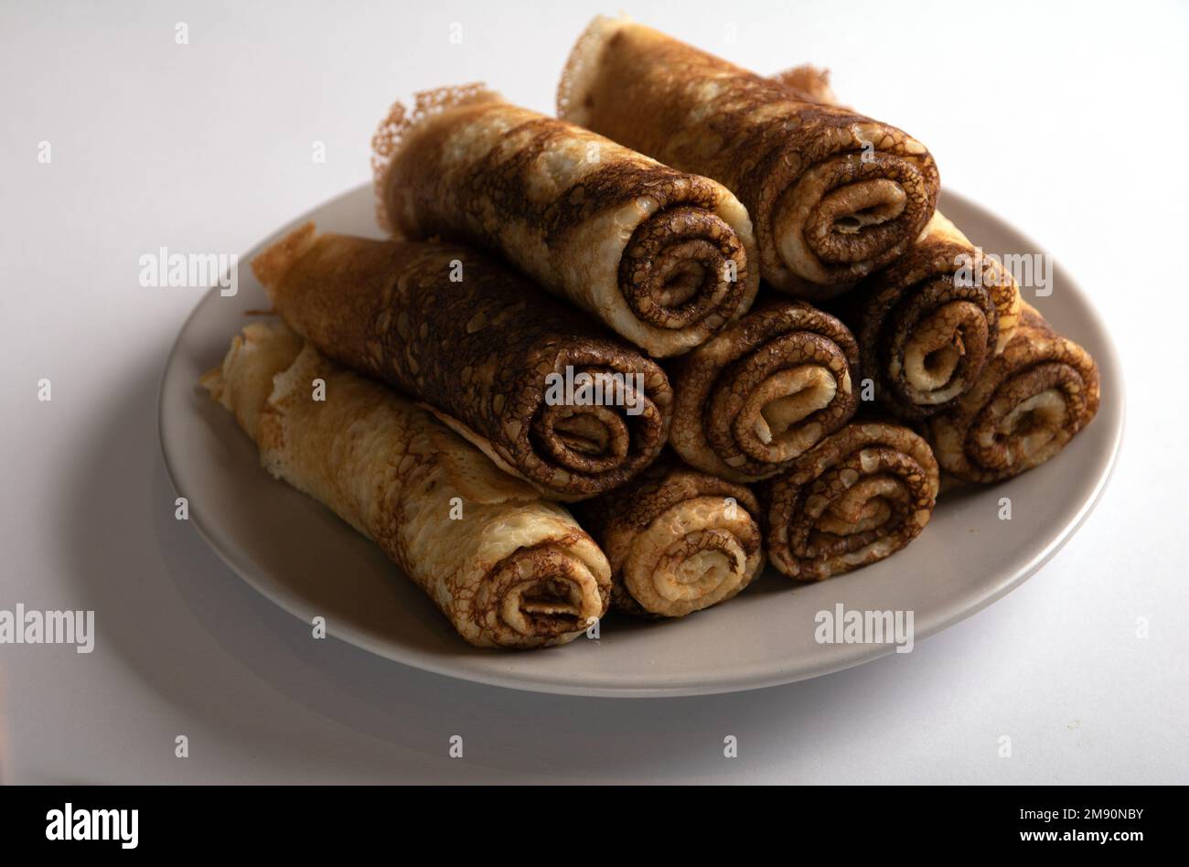 photo pancakes rolled up and lying on a plate on a white background Stock Photo