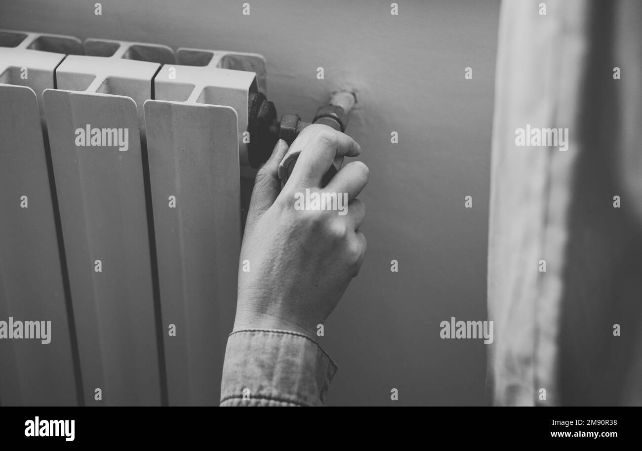Female hand adjusting thermostat to turn on the radiator heater at home. Stock Photo