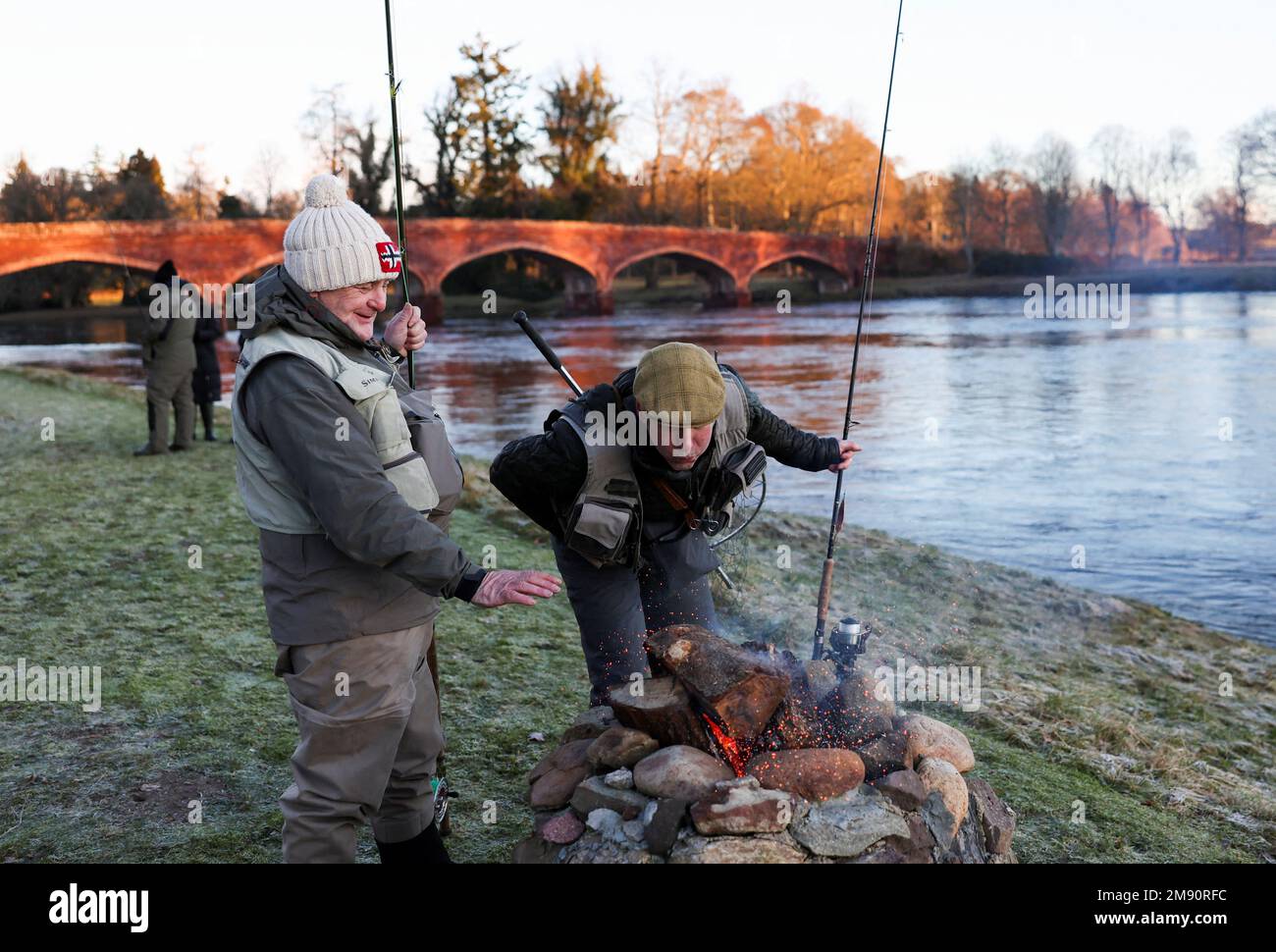 Anglers blow on a fire on the opening day of the salmon fishing season on the river Tay at Meikleour fisheries, Scotland, Britain, January 16, 2023. REUTERS/Russell Cheyne Stock Photo