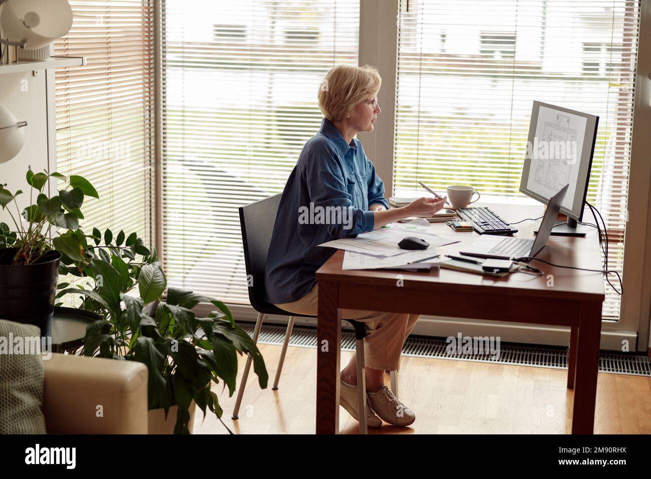 Focused mature woman engineer constructor works on project from home office using computer Stock Photo