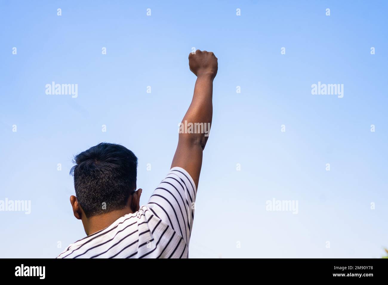 Back view shot of young man raising hand fist against sky - concept of black history month, justice and activism. Stock Photo