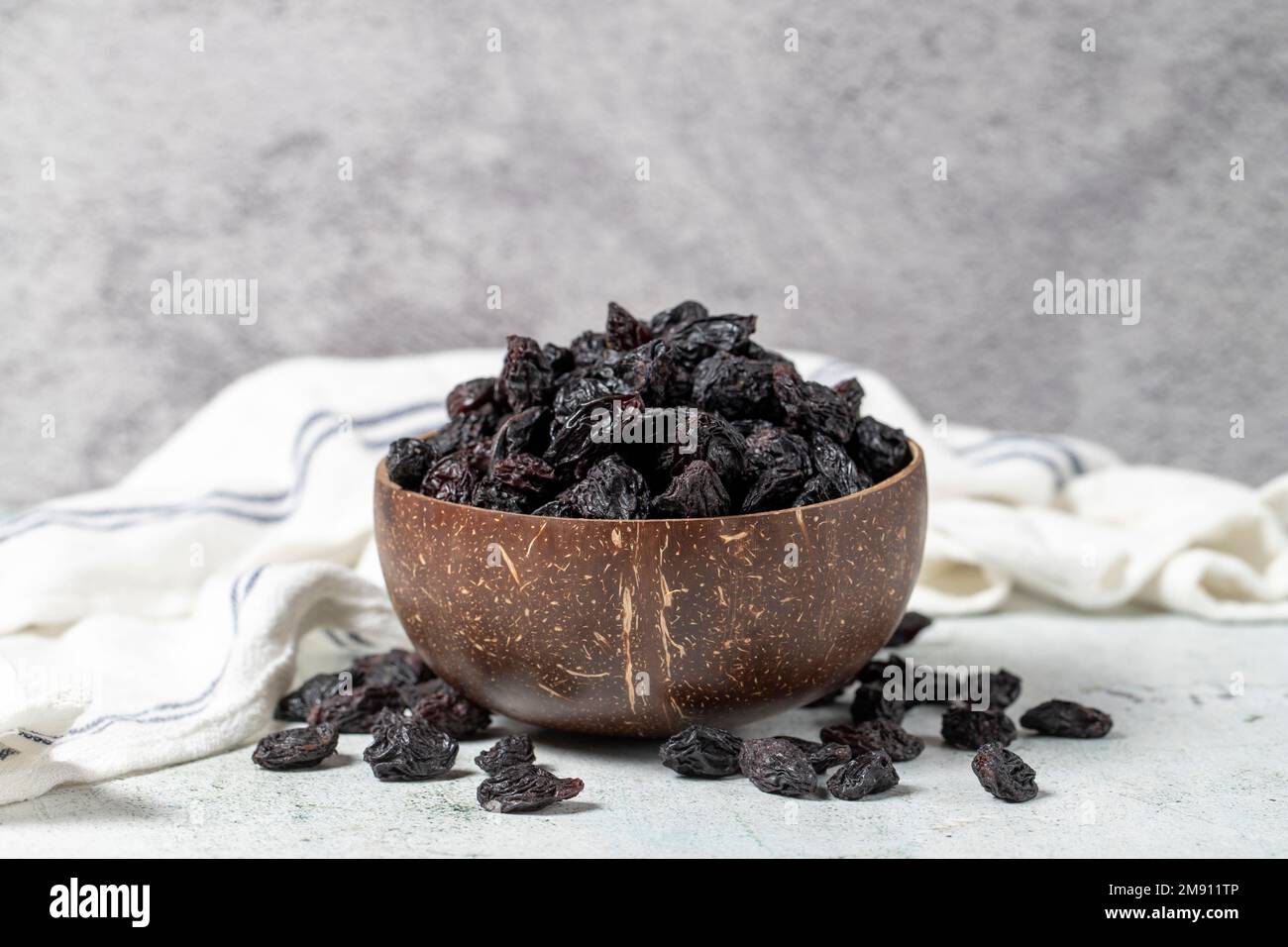 Dried black grapes on stone background. Dried grapes in coconut bowl