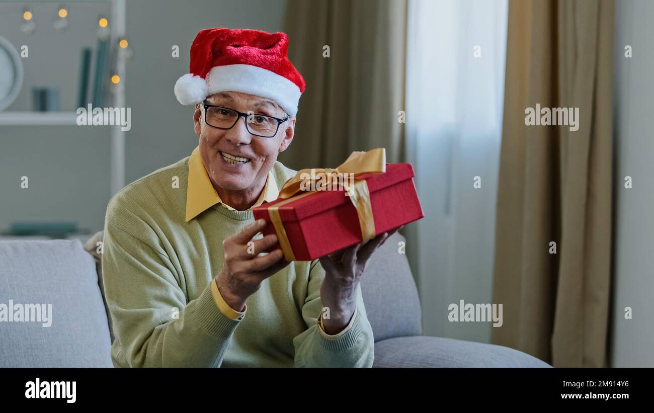 Old Caucasian senior mature man grandfather in Santa Christmas hat at home singing song dancing moving hands having fun celebrating x-mas New Year Stock Photo