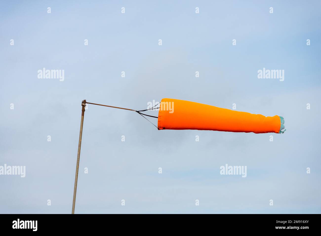 A bright orange windsock being blown horizontally in strong winds by an