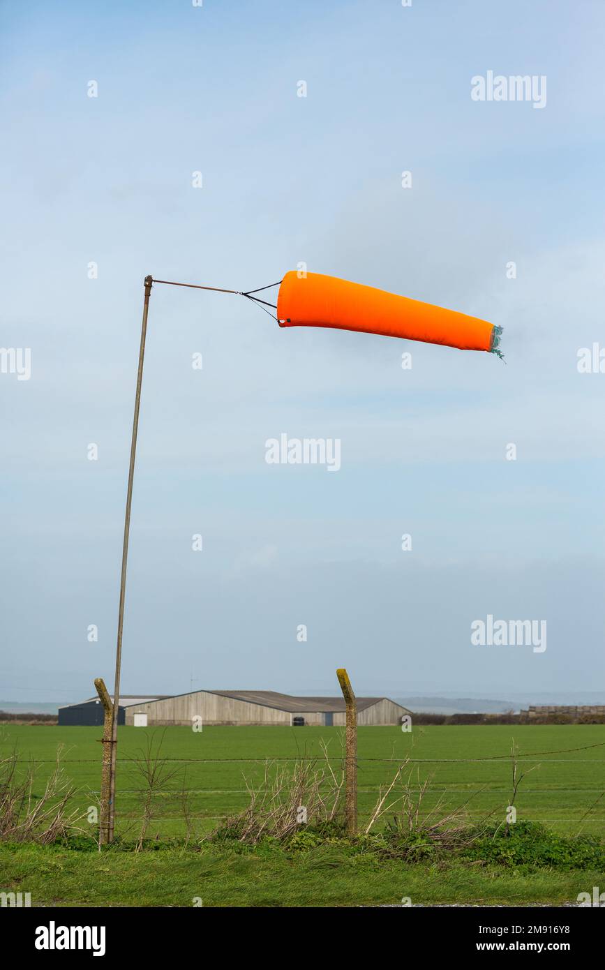 A bright orange windsock being blown horizontally in strong winds by an