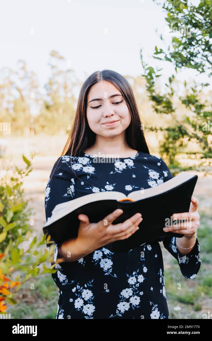 Smiling young religious girl reading her bible, outside in the field at sunset. Spiritual