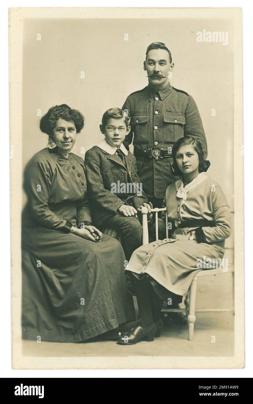 Original WW1 era studio portrait postcard family group posing for a photograph together. The children sit with their mother and father. The girl is of teenage years. All our in their Sunday best clothes. The father is in uniform and is possibly a Royal Marines Light Infantryman as indicated from his belt buckle design. Perhaps the soldier is on leave or about to go to the front. Dated Christmas 1915 on the reverse of the card, U.K. Stock Photo