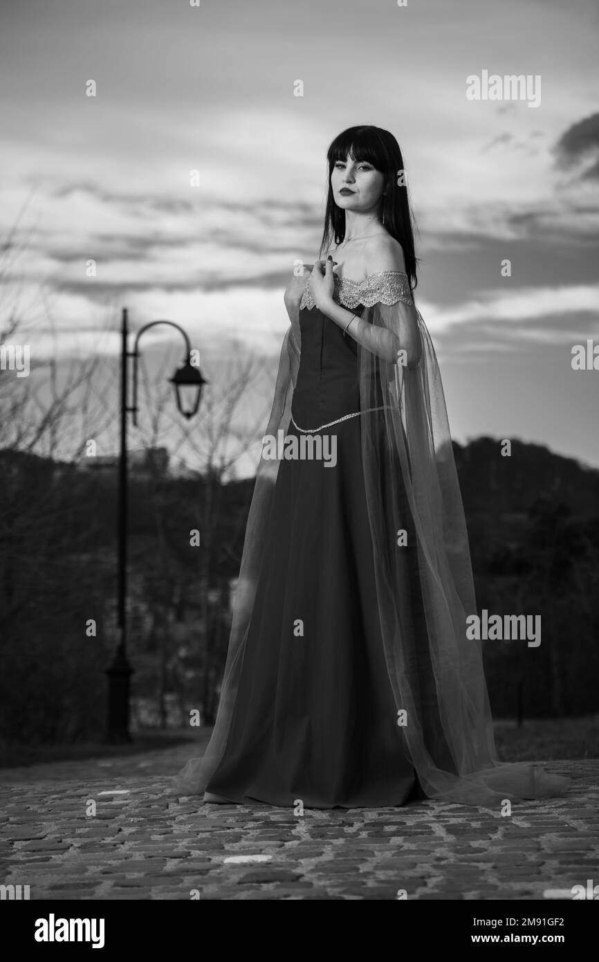 A vertical grayscale shot of a woman wearing a medieval dress posing outdoors Stock Photo
