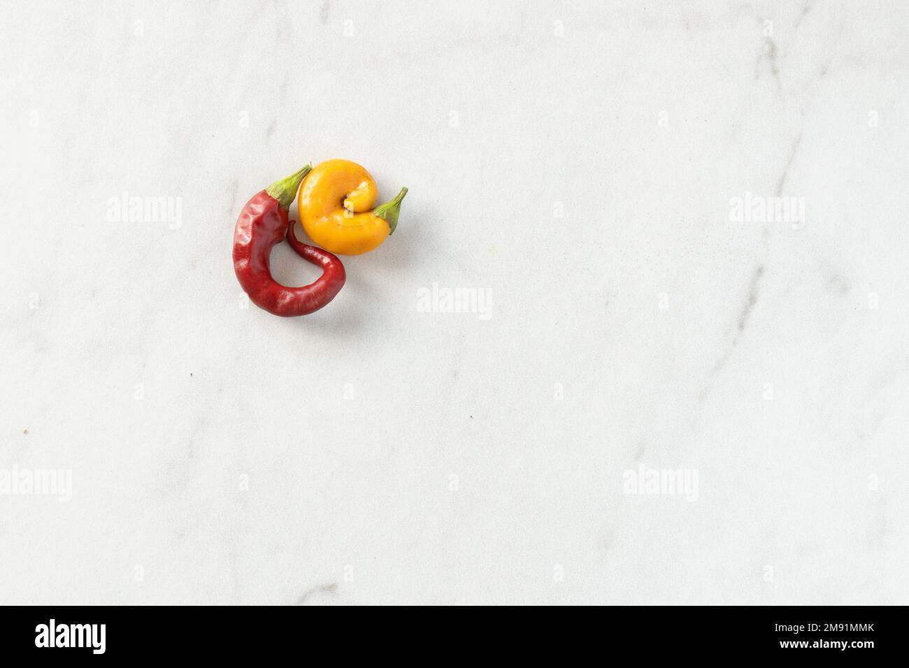 Two curved Thai chile peppers nestled against each other on a white marble counter with copy space; food photography Stock Photo
