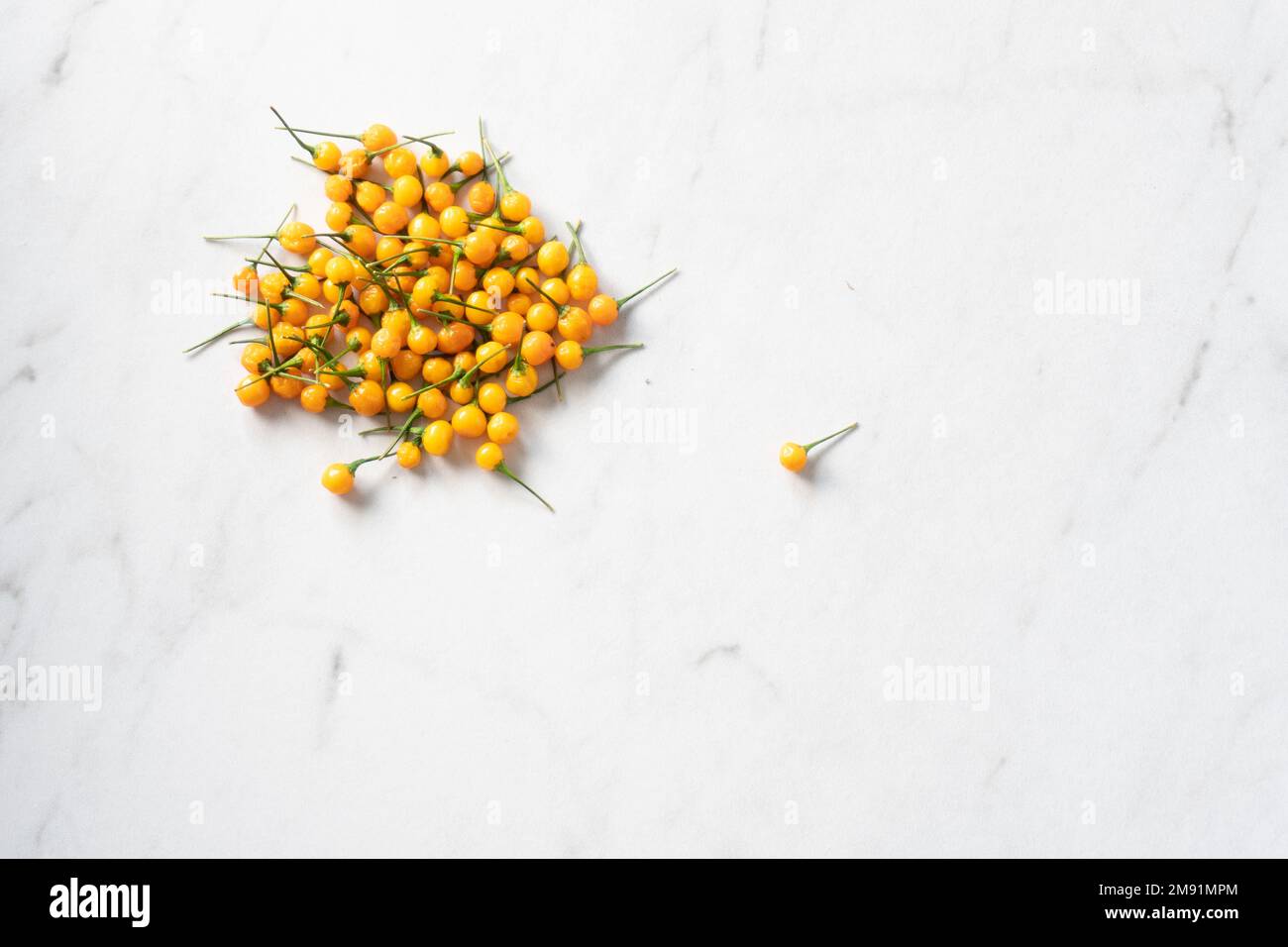 A bright yelllow aji charapita pepper sits apart from a pile on a white marble surface; food photography Stock Photo