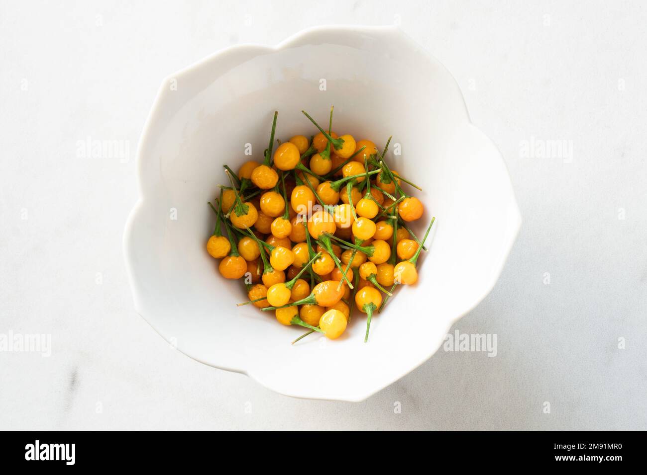 A bowl of bright yellow aji charapita peppers on white marble; food photography Stock Photo