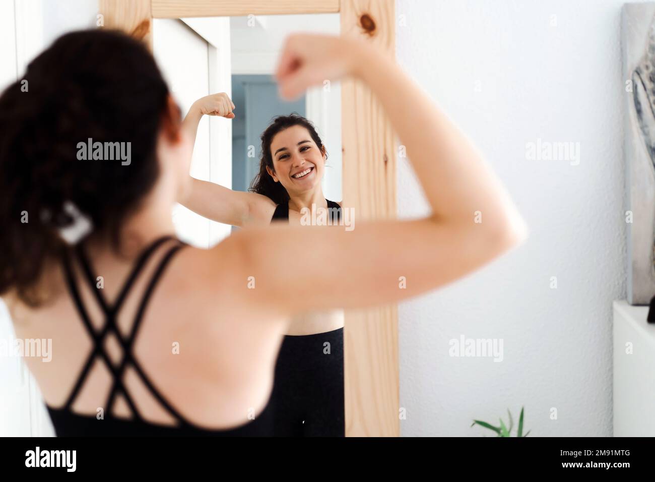 Funny young woman flexing arms looking in the mirror after doing her training Stock Photo