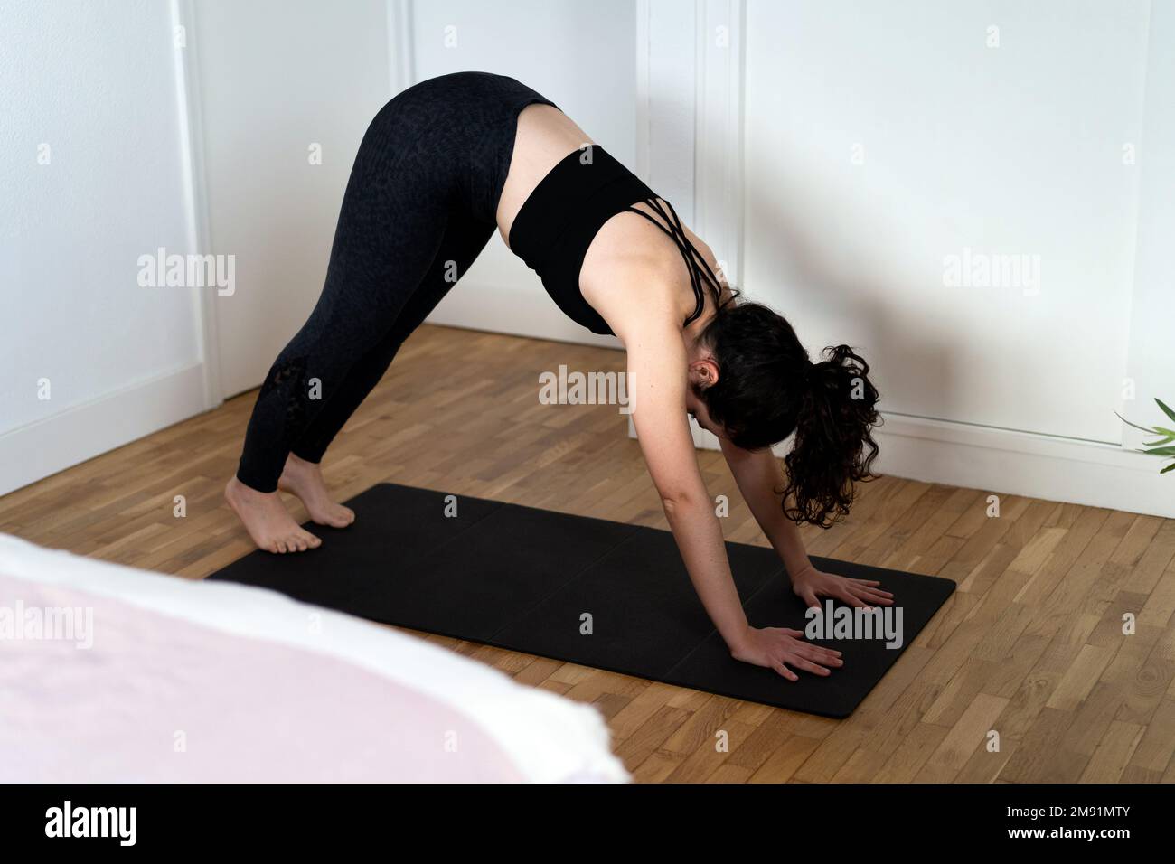 Young woman practising yoga in her bedroom. Adho mukha svanasana position Stock Photo