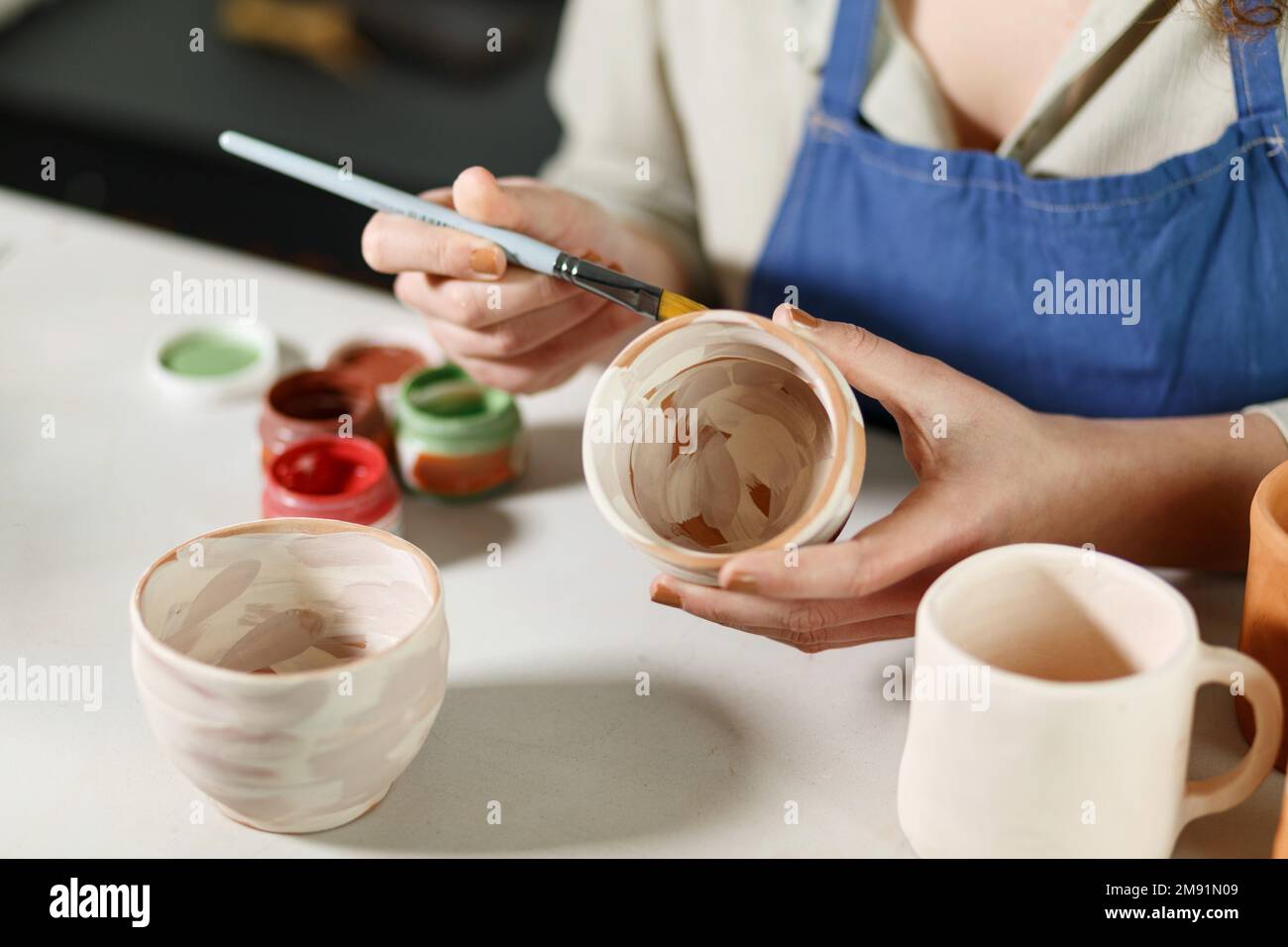 Woman hands, pottery studio and painting cup in workshop for sculpture, creative manufacturing or design. Painter, ceramics product and brush process, Stock Photo