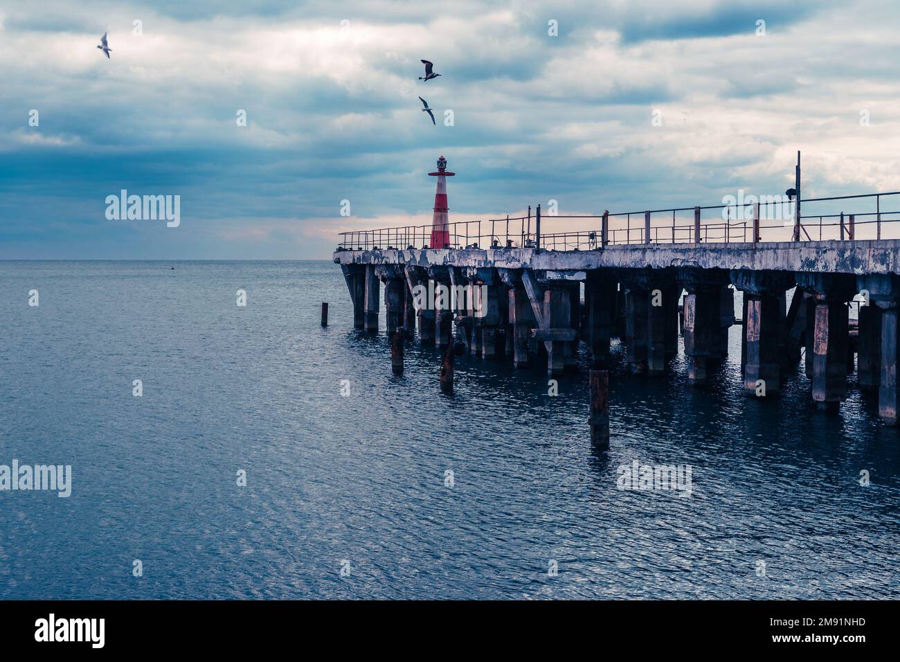 Pier with lighthouse on the Black Sea coast with dramatic sky. Alushta. Crimea Stock Photo