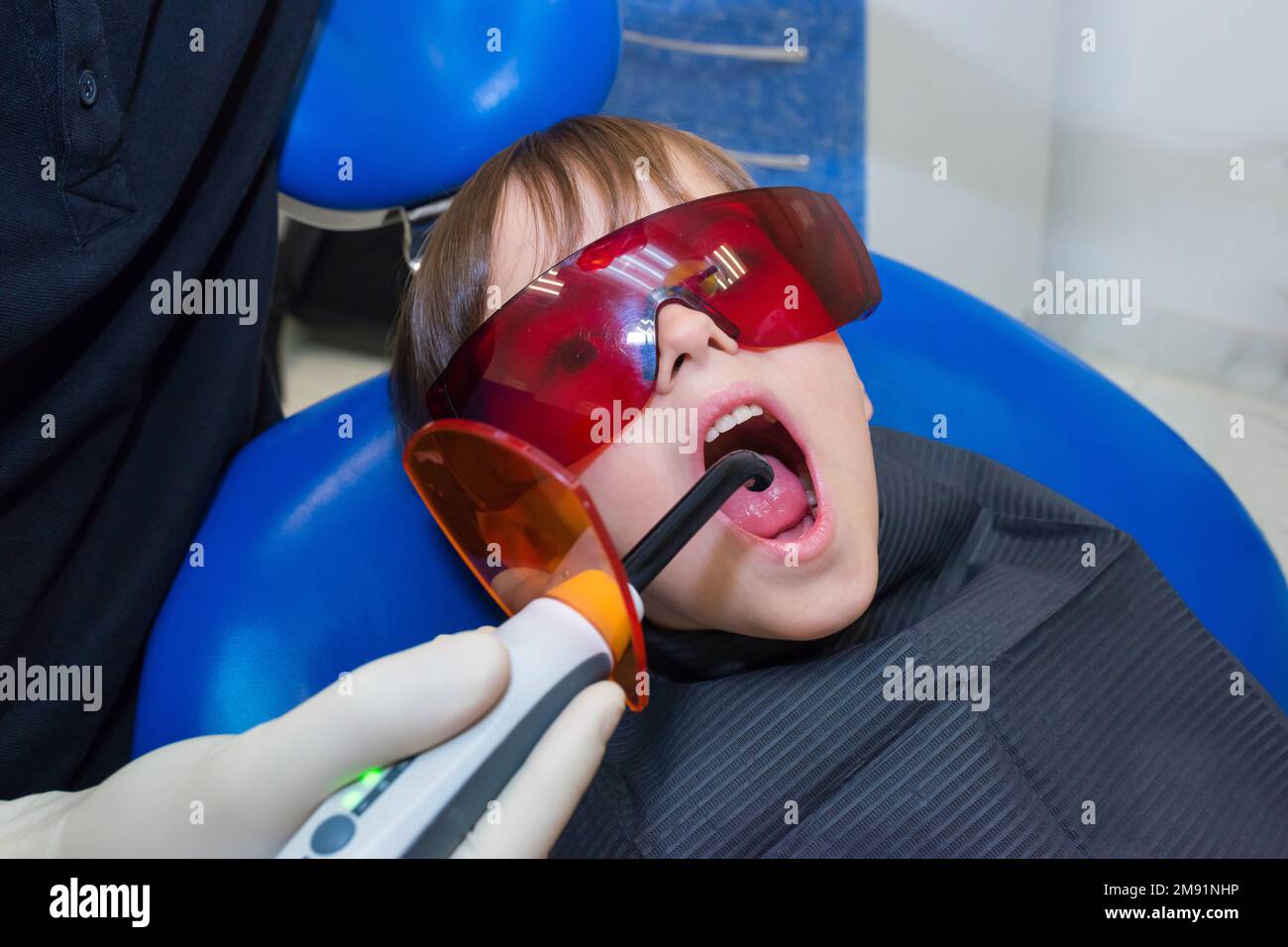 A dentist is examining a child patients teeth with a uv light lamp