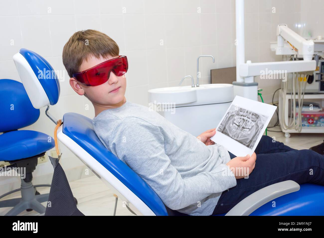 A happy boy in safety glasses with dental X-rays (radiographs) in her hands sitting in a dentist office Stock Photo