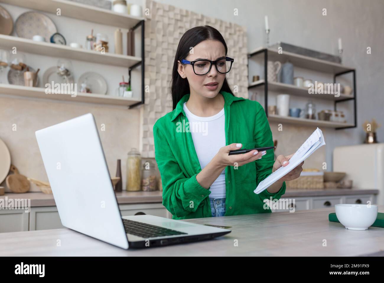 Online business meeting. Young upset woman talking on video call from laptop with tax, bank, creditor. Quarrels, shows a notebook with bills. Stock Photo